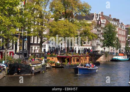 Erkunden Sie den Prinsengracht-Kanal in Amsterdam an einem sonnigen Tag mit lebhaften Bootstouren und üppigen Bäumen. Niederlande, Europa Stockfoto