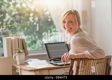 Lächelnde Frau am Schreibtisch sitzen und über die Schulter schauen Stockfoto