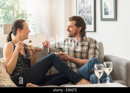 Fröhliches paar Essen auf sofa Stockfoto