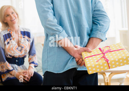 Rückansicht des Menschen halten eingewickelt Geburtstagsgeschenk hinter stehen wieder vor der lächelnde Frau Stockfoto