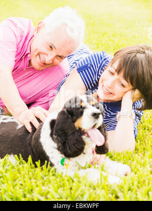 Lächelnde paar mit Hund im Grass liegen Stockfoto