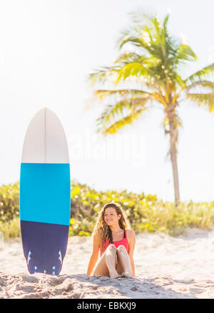 USA, Florida, Jupiter, Portrait von junge Frau sitzt in der Nähe von Surfbrett am Strand Stockfoto
