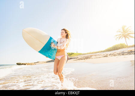 USA, Florida, Jupiter, junge Frau, die ins Meer tragen Surfbrett in Surf ausgeführt Stockfoto