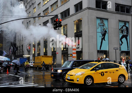 Manhattan New York USA - Dampf steigt aus einem u-Bahn-Rohr in Fifth Avenue im strömenden Regen mit gelben Taxi Stockfoto