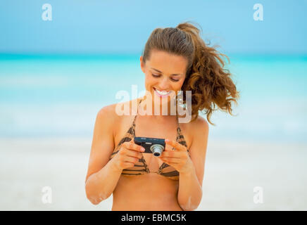 Glückliche junge Frau, die Fotos in der Kamera überprüfen, während am Strand Stockfoto