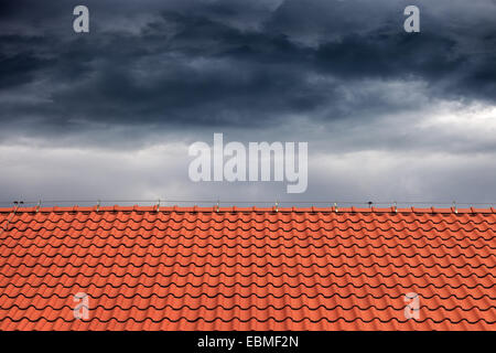 Dunkle Regenwolken über dem Orangen Dach. Stockfoto