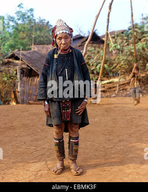 Ältere Frau mit einem Pfiff stand vor Bambushütten in einem Akha Dorf, Provinz Chiang Rai, Nordthailand Stockfoto