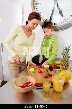 Mutter und Sohn Schneiden von verschiedenen Arten von Obst auf Schneidebrett in der Küche, Deutschland Stockfoto