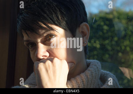Junge Frau mit kurzen dunklen Haaren tief in Gedanken mit dem Kopf in der Hand. Stockfoto