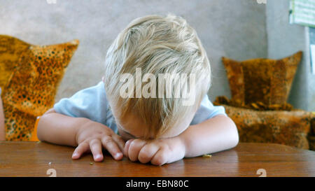 kleiner Junge mit blonden Haaren beim Einschlafen am Schreibtisch Stockfoto