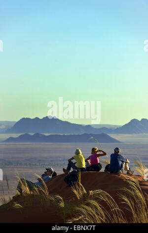 Gruppieren Sie sitzen auf einer Düne in der Wüste und genießen die Aussicht, Namibia, Namib-Naukluft-Nationalpark, Sesriem Camp Stockfoto