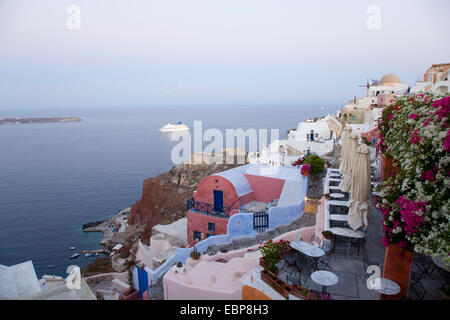 IA, Santorini, südliche Ägäis, Griechenland. Bunte Häuser, klammerte sich an den Hang oberhalb Ammoudi Bucht, Dawn, Kreuzfahrtschiff ankommen. Stockfoto