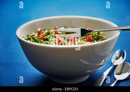 Taboulé Salat in einer weißen Schüssel auf einem dunkelblauen Hintergrund mit silbernen Löffel und einer Gabel serviert Stockfoto