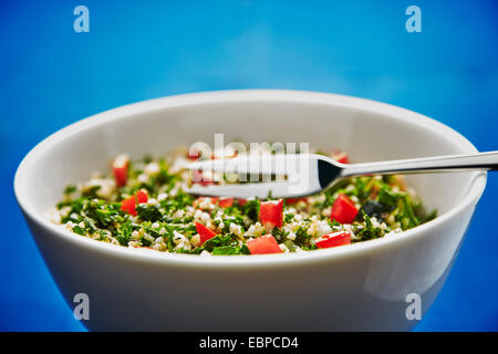 Taboulé Salat in einer weißen Schüssel auf einem dunkelblauen Hintergrund mit silbernen Löffel und einer Gabel serviert Stockfoto