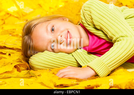 Kleines blondes Mädchen legt auf die herbstliche Ahornblätter Stockfoto