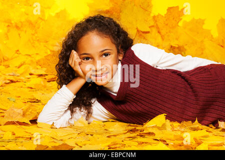 Kleine schwarze Mädchen legt auf die herbstliche Ahornblätter Stockfoto