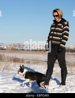 Frau und ihr Boston Terrier Hund genießen es, draußen im Stadtpark in der Natur zu spazieren Stockfoto