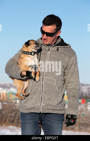 Mann hält seinen Bugg (Kreuzung Boston Terrier und Pug) Hund, während er im Stadtpark spaziert Stockfoto