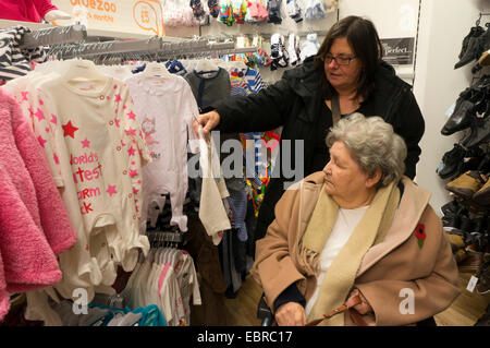 Alte Dame im Rollstuhl und ihre Pfleger oder Assistant Shopping für Baby Kleidung in einem Kaufhaus. Stockfoto