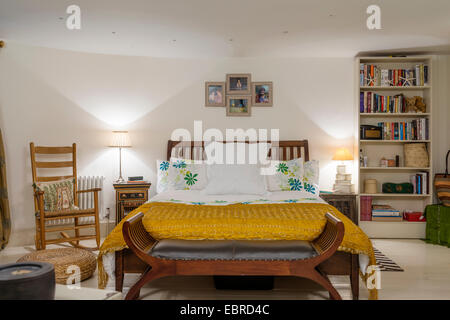 Schaukelstuhl in Schlafzimmer mit gelber Seide Bettdecke und Bücherregal Stockfoto