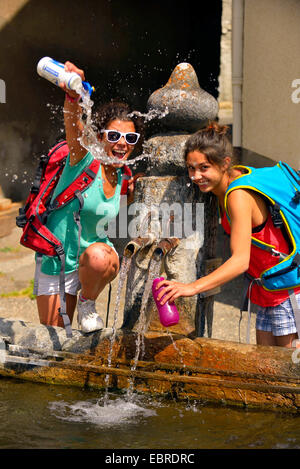 zwei junge weibliche Wanderer erfrischend an einem Brunnen, Frankreich, Savoie Stockfoto