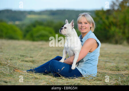 Französische Bulldogge (Canis Lupus F. Familiaris), junge Frau auf einer gemähten Wiese mit eine französische Bulldogge auf dem Schoß, Deutschland Stockfoto