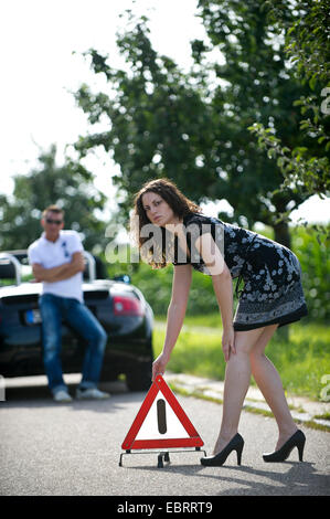 junge Frau, die das Aufstellen von einem Warndreieck mit einem Lächeln nach einer Panne auf einer Landstraße, Deutschland Stockfoto