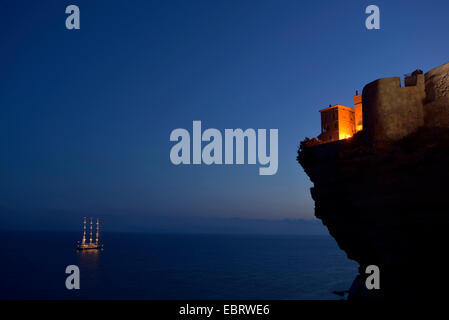 Häuser der alten Stadt am Rande der Kreidefelsen und eine beleuchtete Segelschiff im Abendlicht, Frankreich, Korsika, Bonifacio Stockfoto