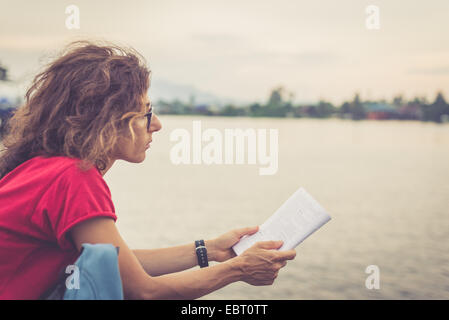 Erwachsene Frau liest Reiseführer Buch bei Sonnenuntergang. Selektiven Fokus. Kreuz verarbeitet mit Vintage Filmeffekt. Warm getönten. Stockfoto