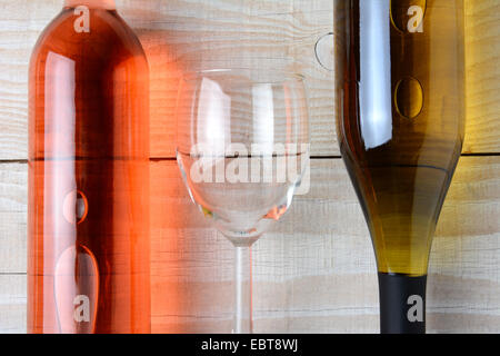 Nahaufnahme eines Weinglases zwischen eine Flasche Rotwein und eine Flasche Weißwein. Alle drei Objekte liegen auf einem rustikalen weiß Stockfoto