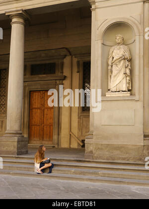 Eine junge Frau mit einer Skizze Pfanne sitzt auf einen Schritt nach oben auf eine Statue in Florenz, Italien. Stockfoto