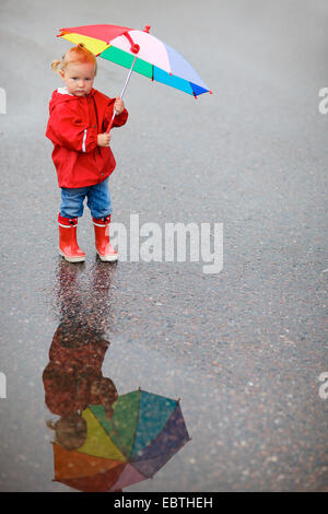 kleines Mädchen in Regenkleidung mit geöffneten Regenschirm Stockfoto