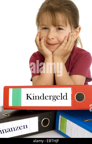 kleines Mädchen lächelnd und stützte sich auf eine Datei mit der Aufschrift "Kindergeld" ("Kindergeld") Stockfoto