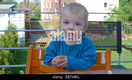 kleiner Junge erlaubte mit Schokolade sitzt auf einem Stuhl auf Terrasse Stockfoto