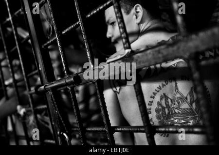 Ein Gang-Mitglied zeigt sein Tattoo hinter den Gittern der Zelle in einem Auffanglager in San Salvador, El Salvador, 20. Februar 2014. Stockfoto