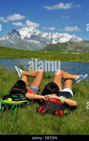 zwei junge Frau liegend auf Bergwiese am See Carolay und genießen Sie einen guten Blick, Frankreich, Nationalpark Vanoise Stockfoto