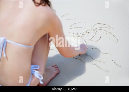 Frau im Bikini, die Zeichnung einer Palme in sand Stockfoto