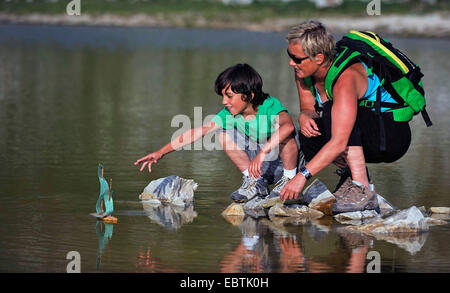 Mutter und Sohn spielen mit einem Spielzeugboot entlang einem Bergsee, Frankreich Stockfoto