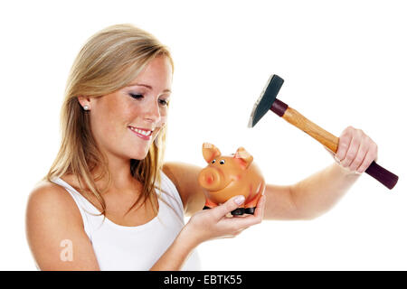 junge Frau mit einem Hammer tötet ihr Sparschwein Stockfoto