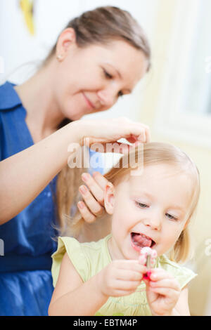 junge Mutter aufsetzen Zöpfe an ihrer kleinen Tochter Stockfoto