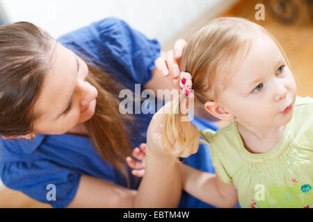 junge Mutter aufsetzen Zöpfe an ihrer kleinen Tochter Stockfoto