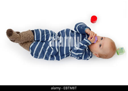 kleines Kind im Strampler auf dem Boden liegen und spielen mit Baby-Spielzeug Stockfoto