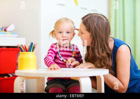 junge Mutter mit ihrer kleinen Tochter zusammen am Tisch sitzen Stockfoto