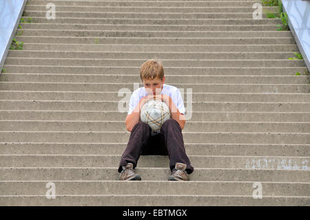 einsame zehn Jahre alter Junge sitzt auf der Treppe mit einem Fußball, Deutschland, Nordrhein-Westfalen, Köln Stockfoto