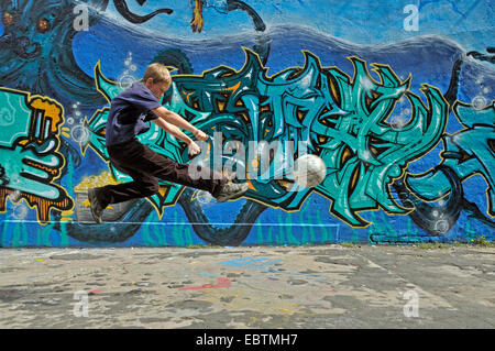 zehn Jahre alten Jungen spielen Fußball vor Graffitiwand, Deutschland Stockfoto