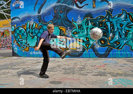 zehn Jahre alten Jungen spielen Fußball vor Graffitiwand, Deutschland Stockfoto