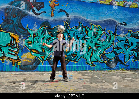 zehn Jahre alten Jungen spielen Fußball vor Graffitiwand, Deutschland Stockfoto