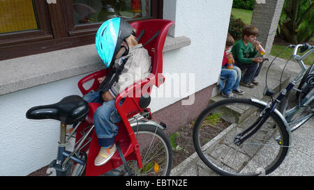 drei kleine Jungen, die nach der Rückkehr von einer Fahrradtour: zwei trinken, man schläft in den Kindersitz auf dem Fahrrad Stockfoto