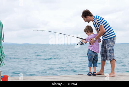 junger Vater und Sohn zusammen Angeln vom Holzsteg Stockfoto