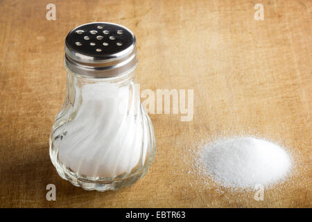 Traditionelle Glas Salzstreuer und verschüttetes Salz auf Holz Hintergrund Stockfoto